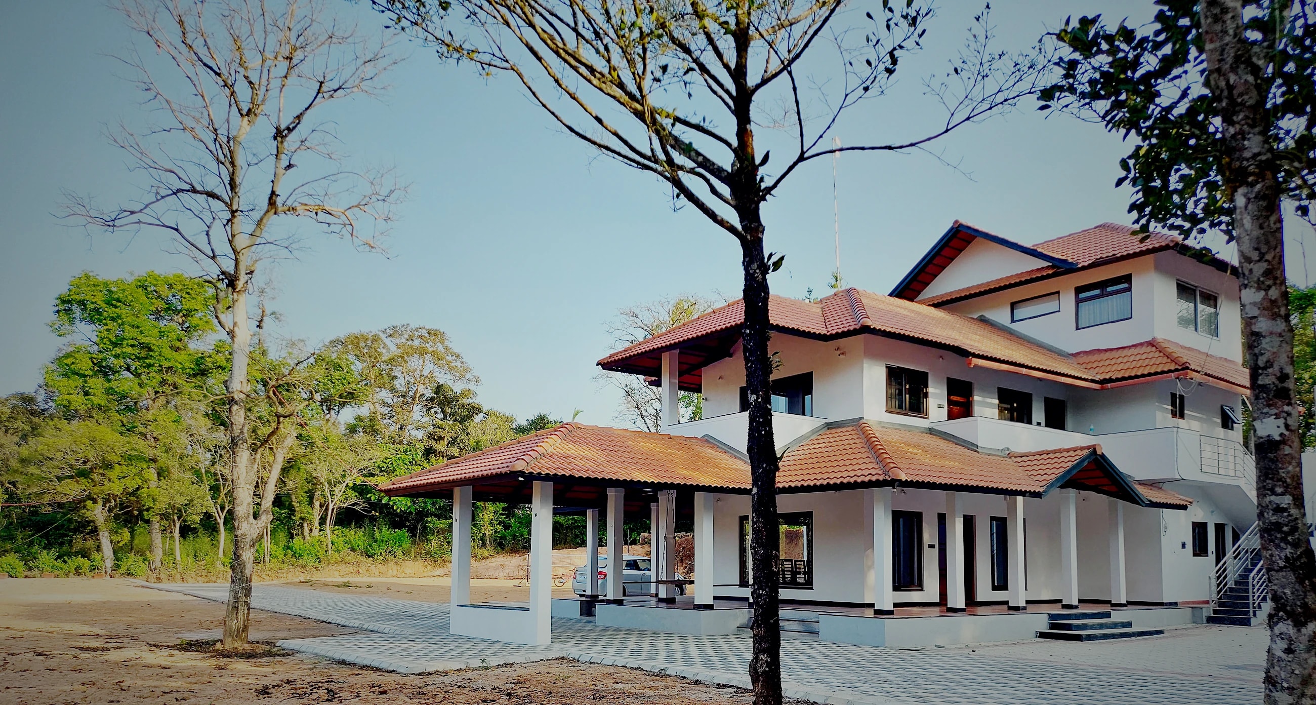 A two-storey, tile-roofed homestay among tall trees on the estate
